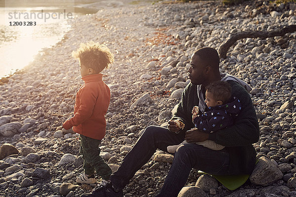 Vater sitzend mit Söhnen auf Felsen am Strand