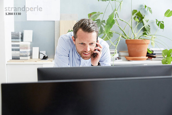 Lächelnder Geschäftsmann beim Telefonieren mit dem Computer im Kreativbüro
