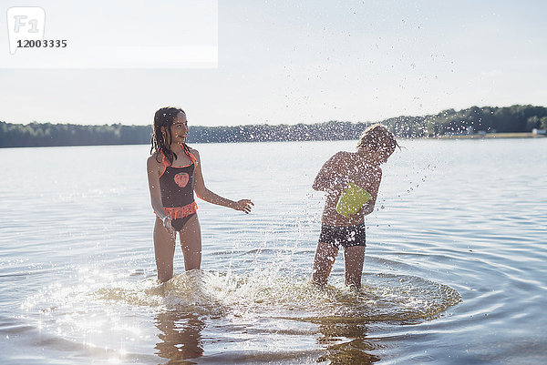 Junge und Mädchen spritzen mit Wasser am Seeufer