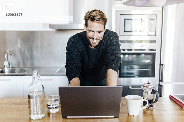 Porträt eines lächelnden Mannes in der Küche mit Laptop