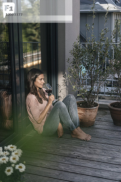 Frau mit einem Glas Rotwein entspannt auf dem Balkon