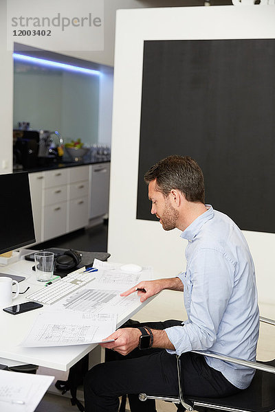 Seitenansicht des Architekten bei der Analyse von Bauplänen am Schreibtisch im Kreativbüro