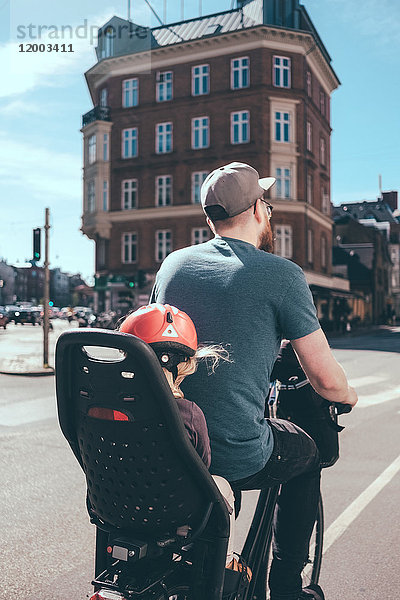 Rückansicht des Vaters beim Radfahren  während die Tochter auf dem Rücksitz in der Stadt sitzt.