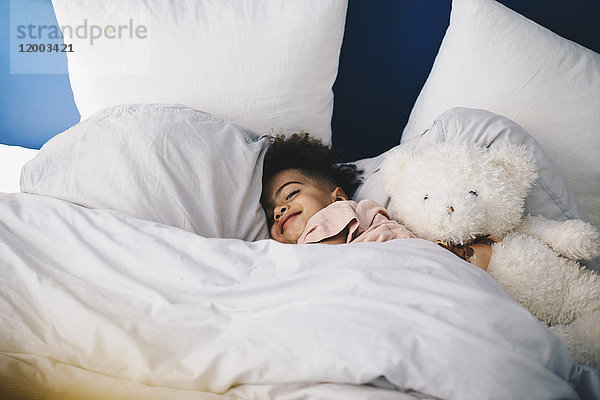 Lächelnder Junge schläft mit Teddybär auf dem Bett zu Hause