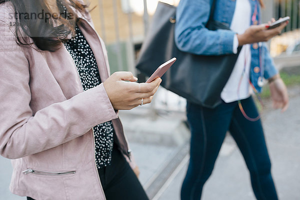 Mittelteil der weiblichen Freunde  die Smartphones benutzen  während sie in der Stadt spazieren gehen.