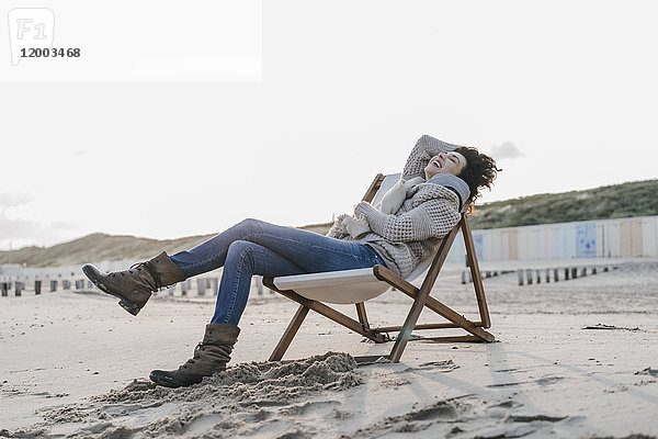 Glückliche Frau sitzt auf dem Liegestuhl am Strand