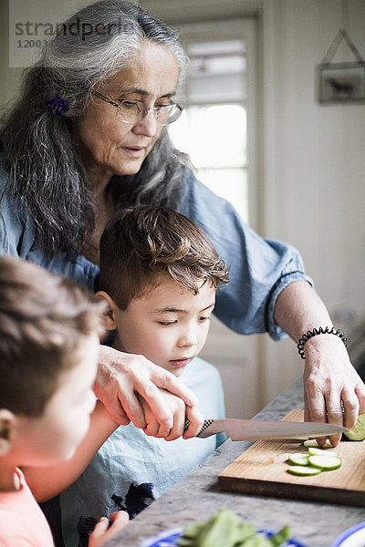 Großmutter hilft Enkel beim Gurkenschneiden in der Küche zu Hause