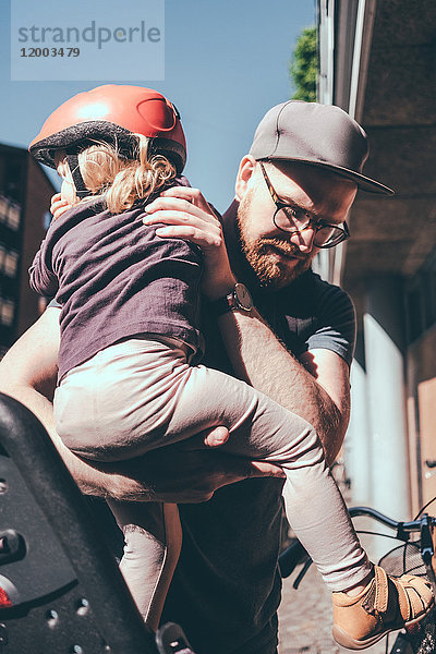 Vater setzt Mädchen auf den Rücksitz des Fahrrads im Freien