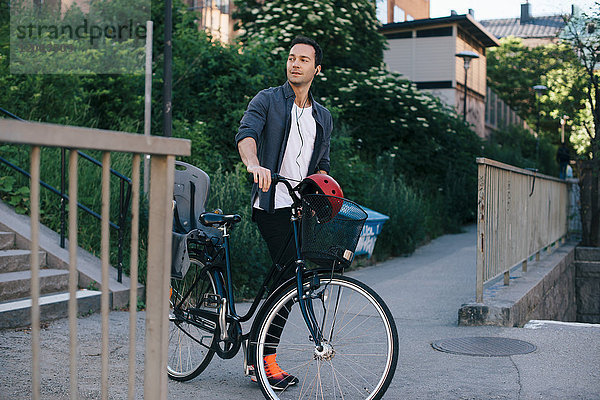 Mittlerer Erwachsener Mann  der mit dem Fahrrad auf einem Fußweg in der Stadt spazieren geht.
