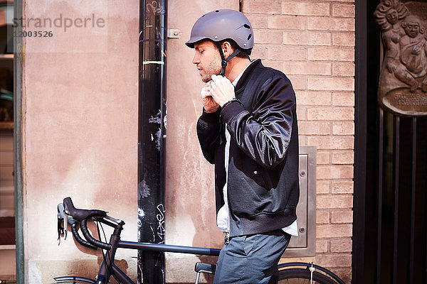 Seitenansicht des Geschäftsmannes mit Helm beim Sitzen auf dem Fahrrad an der Wand in der Stadt