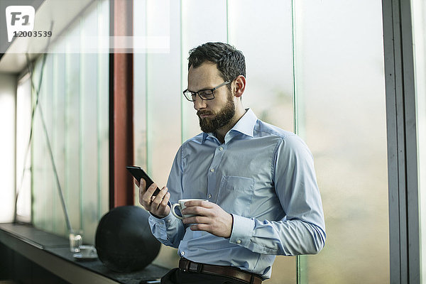 Vielbeschäftigter Geschäftsmann im Büro mit Smartphone
