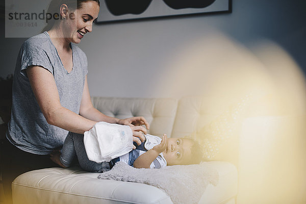 Lächelnde Mutter beim Ankleiden des Jungen auf dem Sofa zu Hause