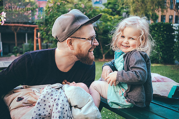 Glücklicher Vater sieht die Tochter an  während er den Sohn im Park hält.