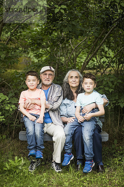 Porträt von Großeltern  die mit Zwillingseltern auf einer Bank gegen Pflanzen im Garten sitzen.