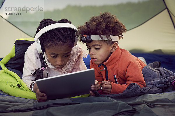 Geschwister im Zelt liegend mit digitalem Tablett