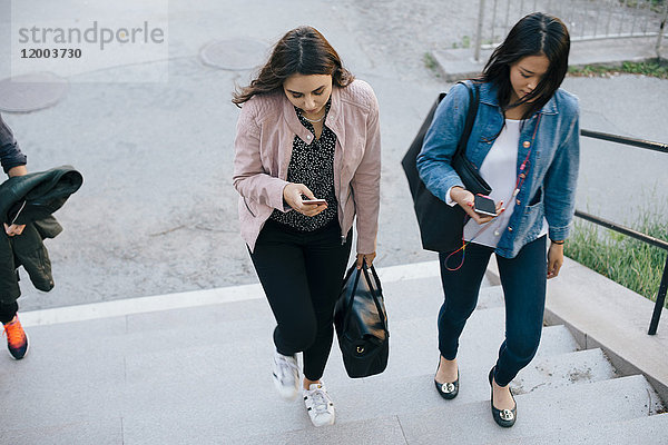 Hochwinklige Ansicht der weiblichen Freunde  die sich auf der Treppe bewegen  während sie Smartphones benutzen.
