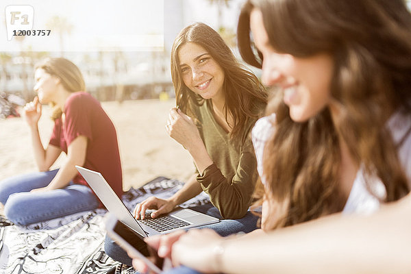 Porträt der lächelnden jungen Frau mit Freunden am Strand mit Laptop