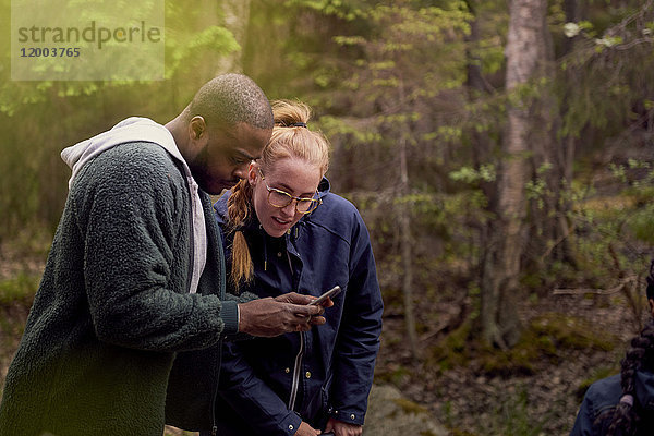 Mann zeigt Smartphone im Stehen mit Tochter im Wald