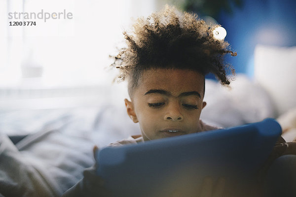 Nahaufnahme des Jungen mit dem digitalen Tablett auf dem Bett zu Hause