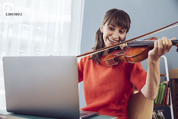 Frau benutzt Laptop zum Spielen eines Liedes auf einer Geige