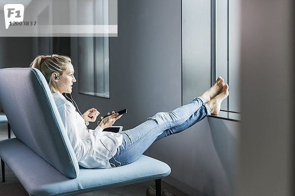 Geschäftsfrau auf der Couch sitzend mit erhobenen Füßen per Handy