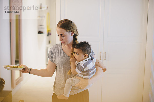 Mutter  die den Sohn trägt  während sie den Teller zu Hause hält.