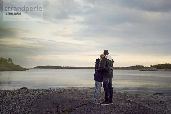 Rückansicht des am Strand stehenden Paares mit Blick auf den See gegen den Himmel bei Sonnenuntergang