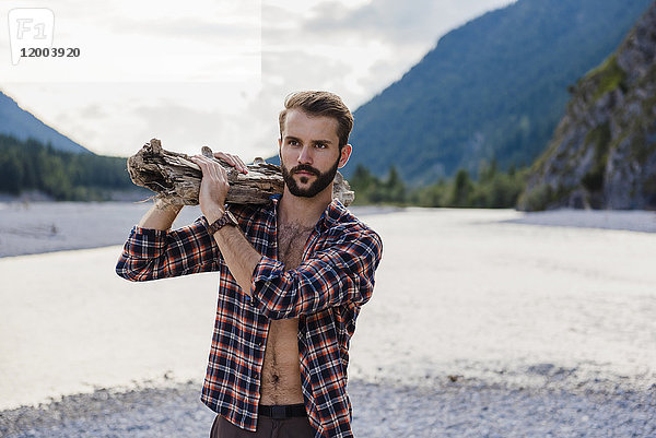 Deutschland  Bayern  Porträt eines jungen Mannes mit Brennholz auf der Schulter in der Natur