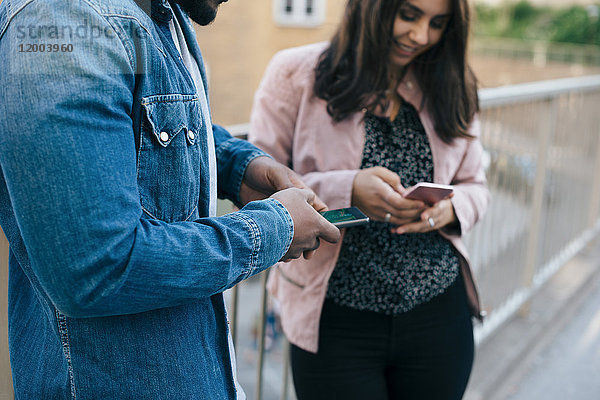 Mittelteil des Mannes  der bei der Benutzung von Smartphones auf der Fußgängerbrücke in der Stadt neben der Frau steht.