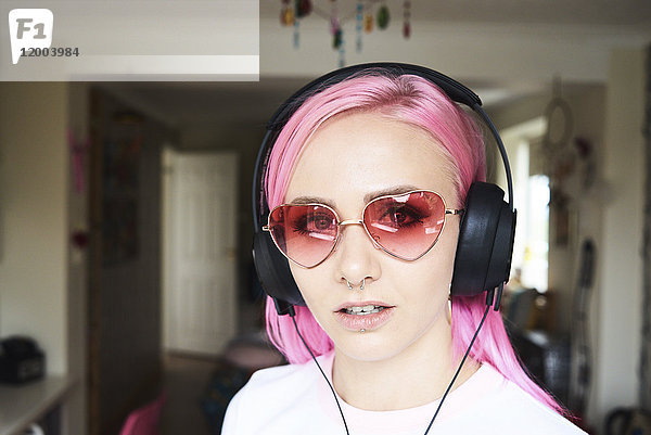 Porträt einer jungen Frau mit rosa Haaren und herzförmiger Sonnenbrille beim Musikhören