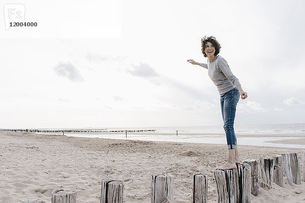 Glückliche Frau balanciert auf Holzpfahl am Strand