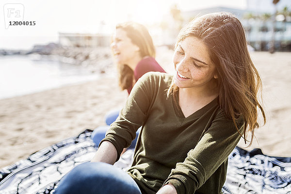 Zwei glückliche junge Frauen sitzen am Strand.