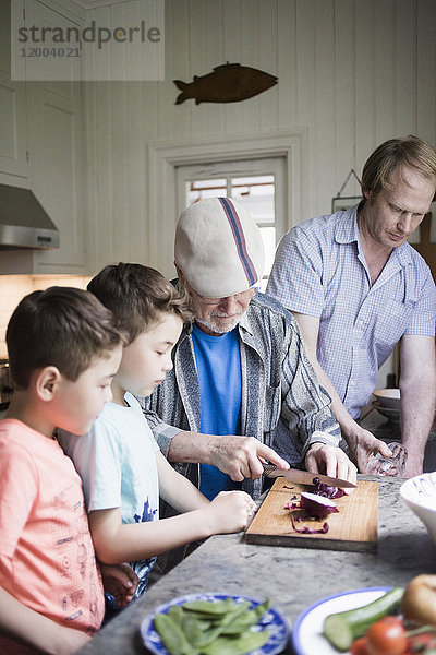 Enkel sehen Großvater beim Zwiebelschneiden an Bord  während der Vater in der Küche arbeitet.