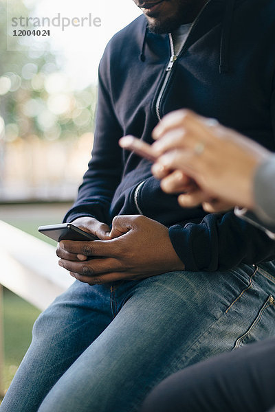 Mittelteil junger multiethnischer Freunde  die Smartphones benutzen  während sie auf dem Geländer sitzen.