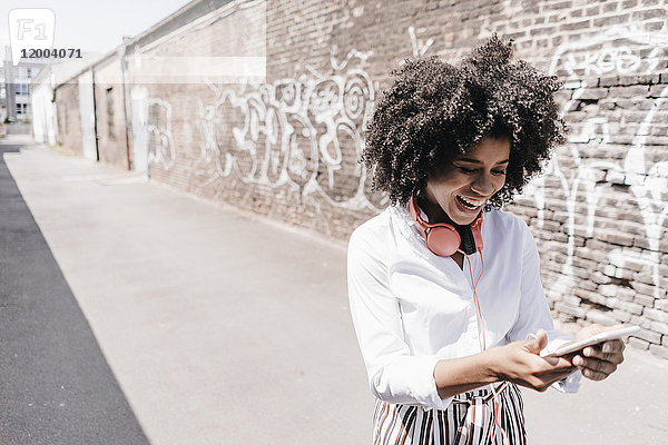 Fröhliche junge Frau beim Blick auf das Handy im Freien