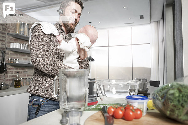 Vater mit Kopfhörer in der Küche hält Baby