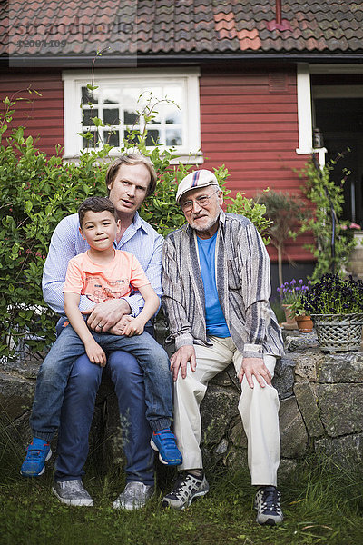 Porträt eines Mannes  der mit Vater und Sohn gegen das Haus im Hinterhof sitzt.