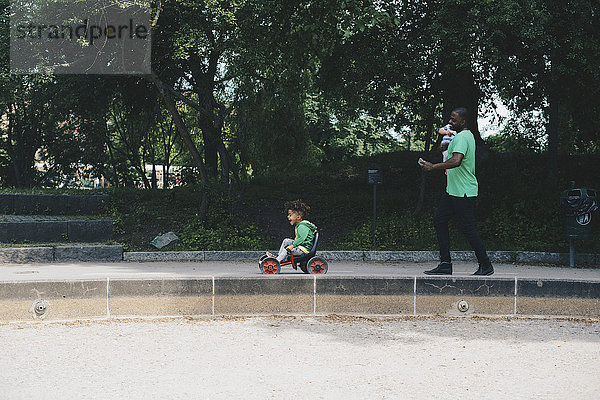 Vater mit Kleinkind und Spaziergang mit Sohn auf dem Dreirad im Park