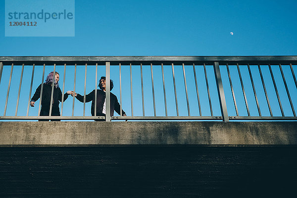 Niedriger Blickwinkel von Freunden  die sich beim Stehen auf der Brücke gegen den klaren Himmel unterhalten