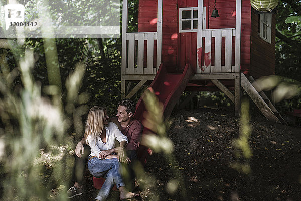 Glückliches Paar sitzt auf der Rutsche eines Gartenschuppens im Wald