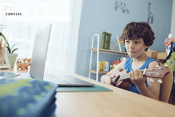 Junge benutzt Laptop  um einen Song auf einer Ukulele zu spielen.