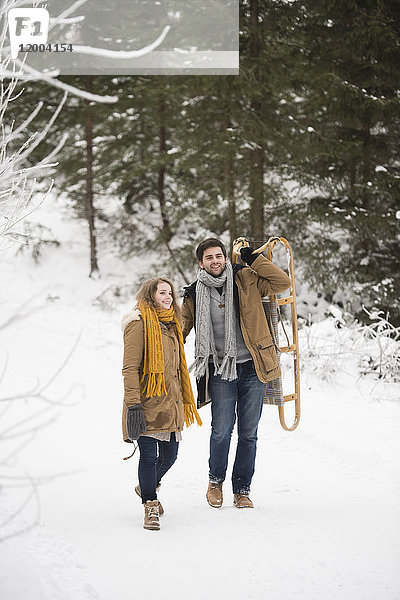 Glückliches junges Paar mit Schlitten im Winterwald