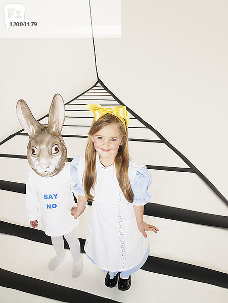 Porträt eines lächelnden Mädchens verkleidet als Alice im Wunderland Hand in Hand mit Mädchen mit Kaninchenmaske