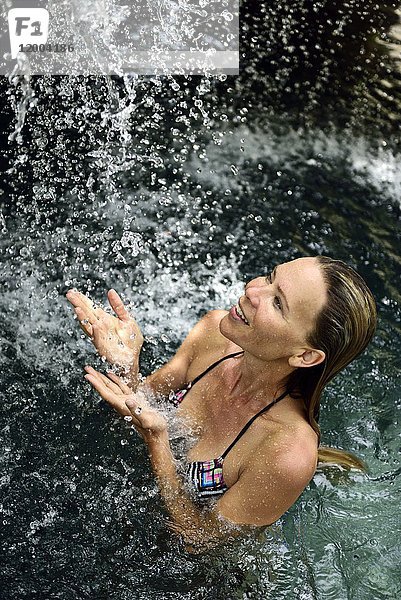 Glückliche Frau im Naturpool mit Wasserfall