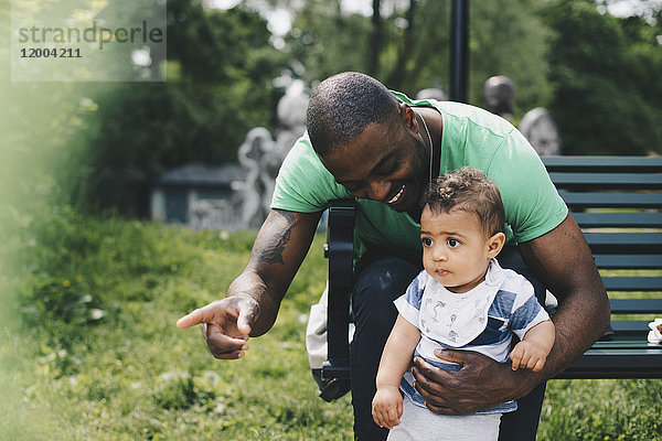 Vater zeigt und zeigt dem Kleinkind  während er auf der Bank im Park sitzt.