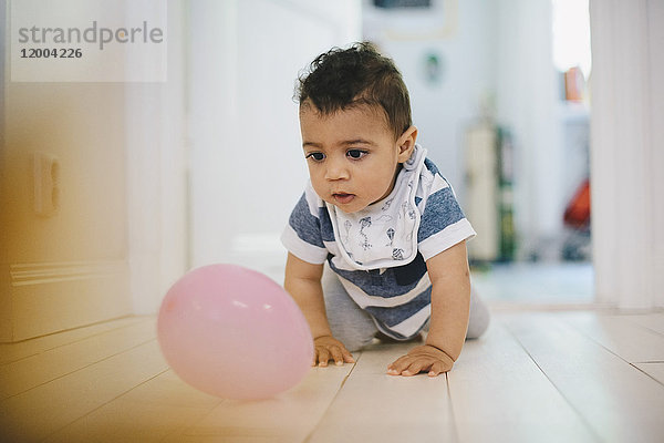 Kleinkind spielt mit dem Ballon  während es zu Hause auf dem Boden krabbelt.