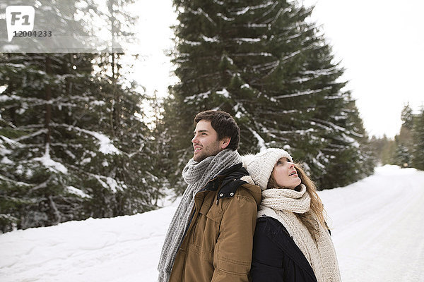 Glückliches junges Paar steht Rücken an Rücken in schneebedeckter Winterlandschaft
