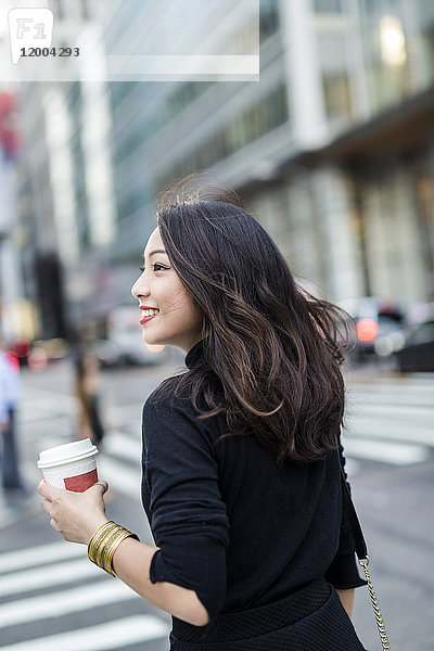 USA  New York City  Manhattan  lächelnde junge Frau mit Kaffee zum Überqueren der Straße