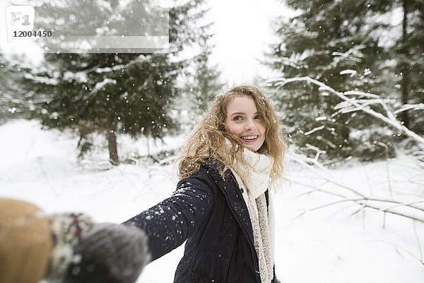 Porträt einer glücklichen jungen Frau  die im Winterwald die Hand hält