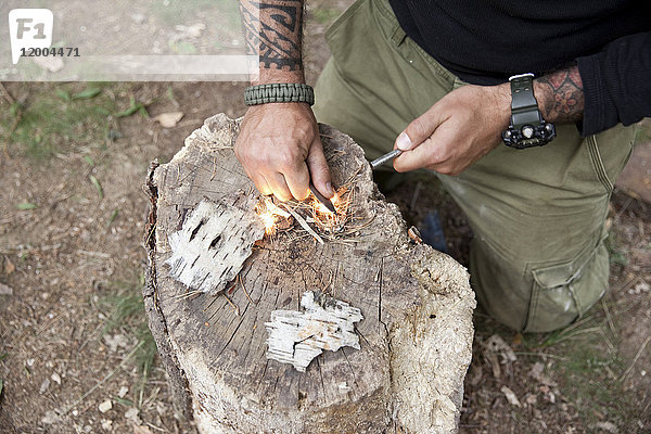 Mann entzündet ein Feuer auf Baumstumpf im Wald